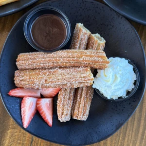 Warm cinnamon sugar churros served with chocolate dipping sauce, whipped cream, and fresh strawberries at The Coffee Garden in the Heights, Houston TX 77007.